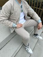 Man zit op traptrede terwijl hij een beige bomberjack draagt met witte t=shirt en beige broek, voorzijde close-up.