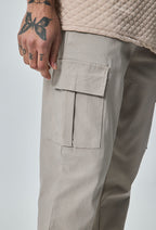 Close-up van beige heren cargo broek met cargozak aan de zijkant en detail van de stof.