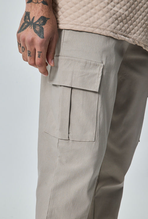Close-up van beige heren cargo broek met cargozak aan de zijkant en detail van de stof.