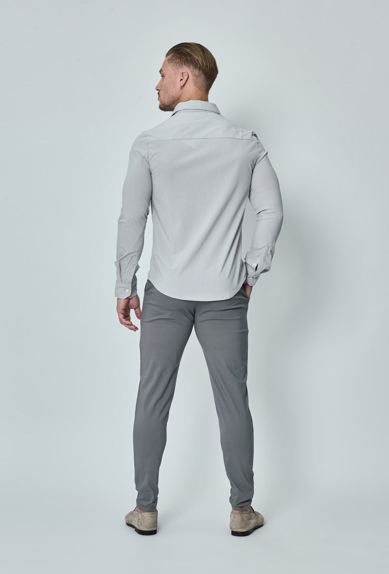 Achterkant van donkergrijze chino broek, model staat recht met handen naast het lichaam.