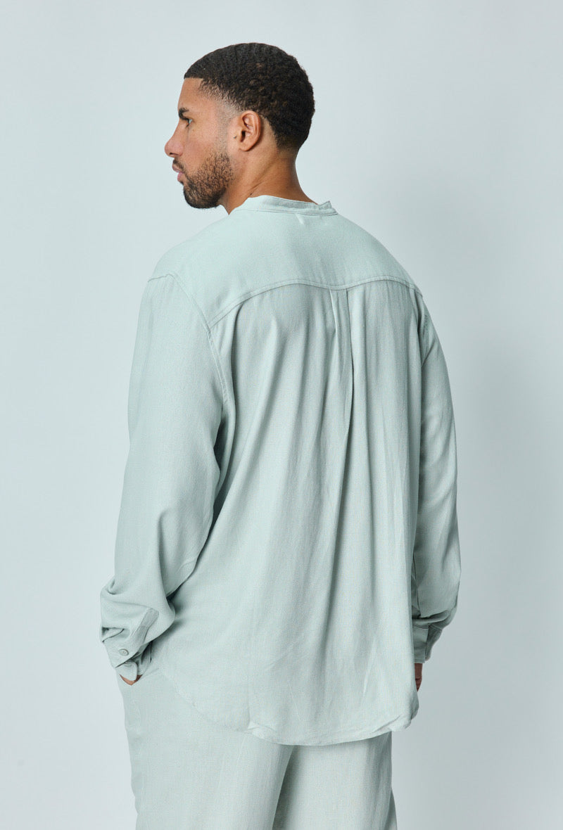 Achterkant van herenmodel met lichtblauwe linnen set, losvallend overhemd en rechte broek.