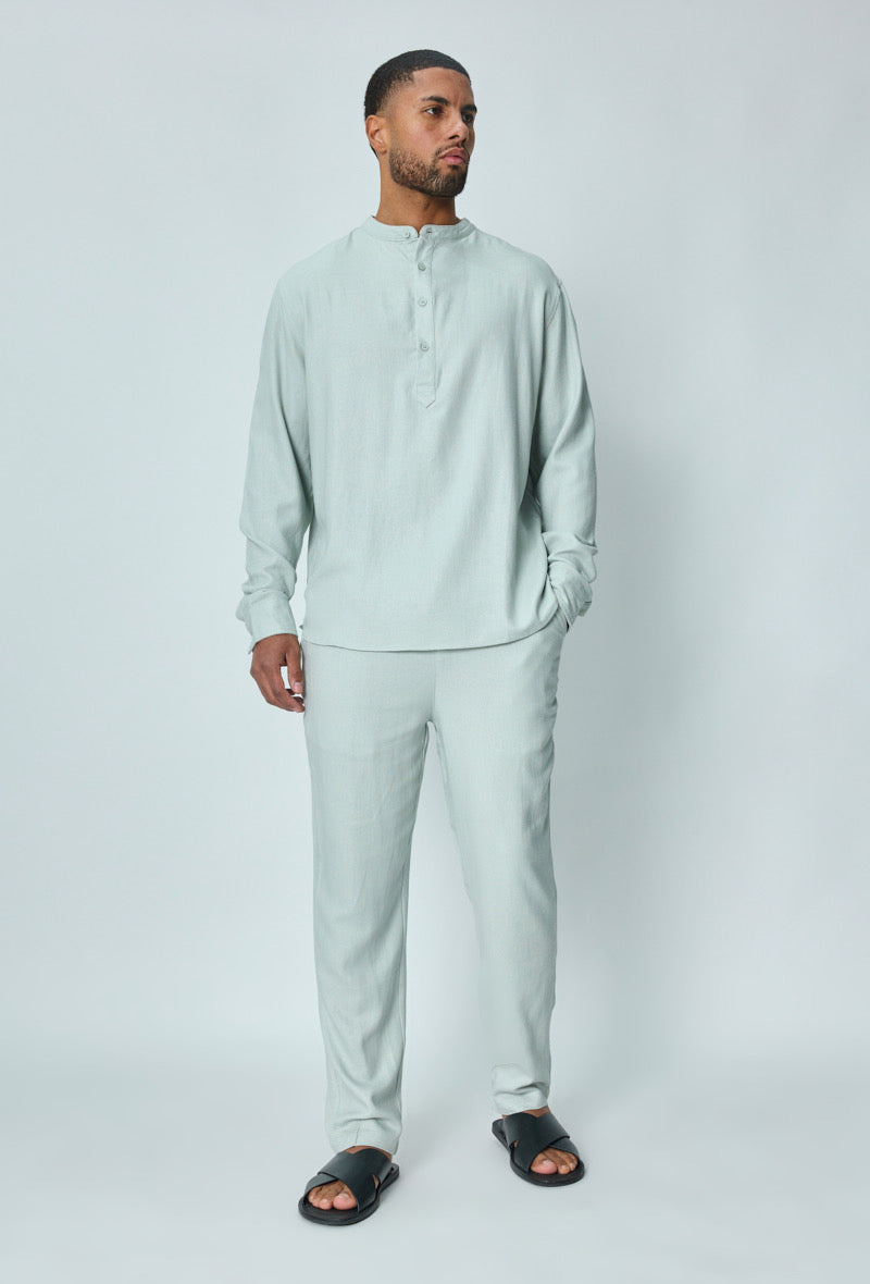 Herenmodel draagt een lichtgrijze linnen set met overhemd en broek, frontaal gefotografeerd.