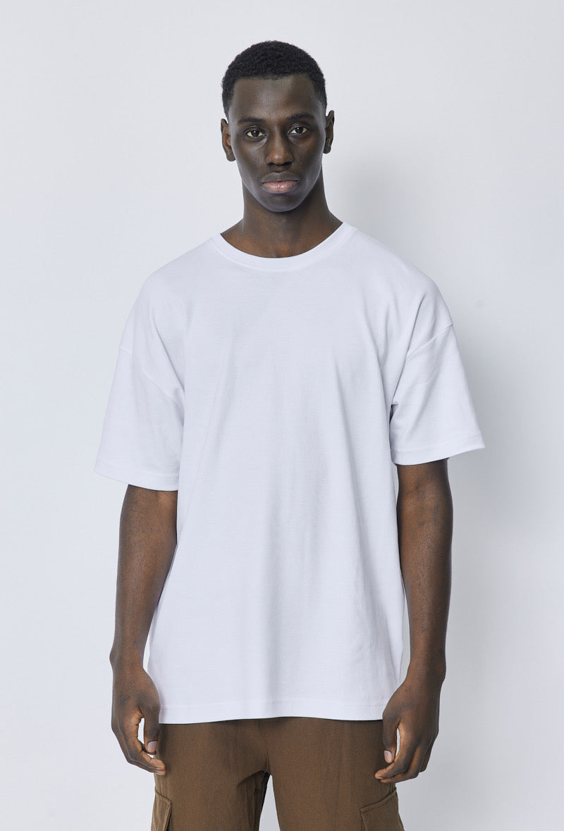 Model draagt een wit oversized T-shirt, frontaal zicht tegen neutrale achtergrond.