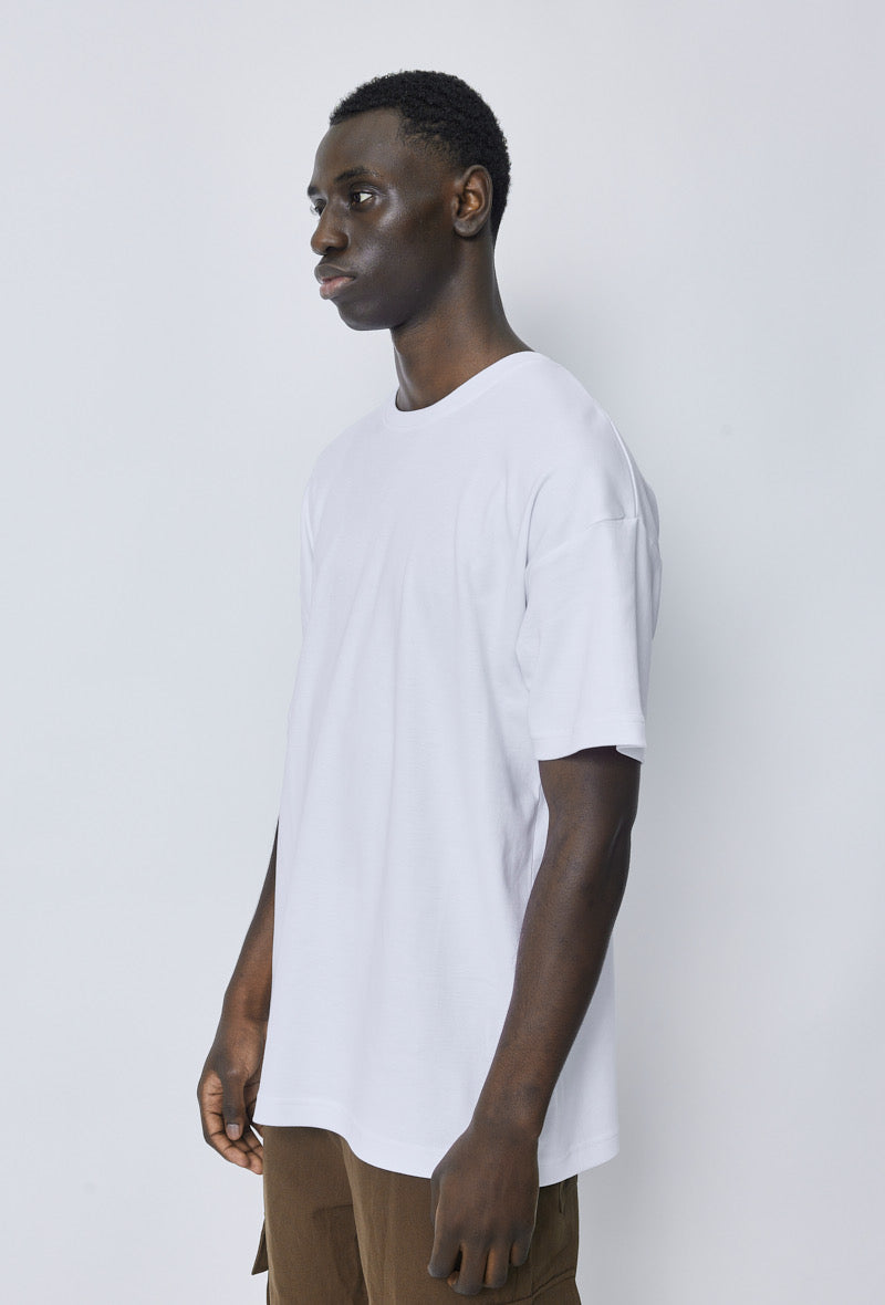 Zijaanzicht van model met wit oversized T-shirt, ontspannen houding.