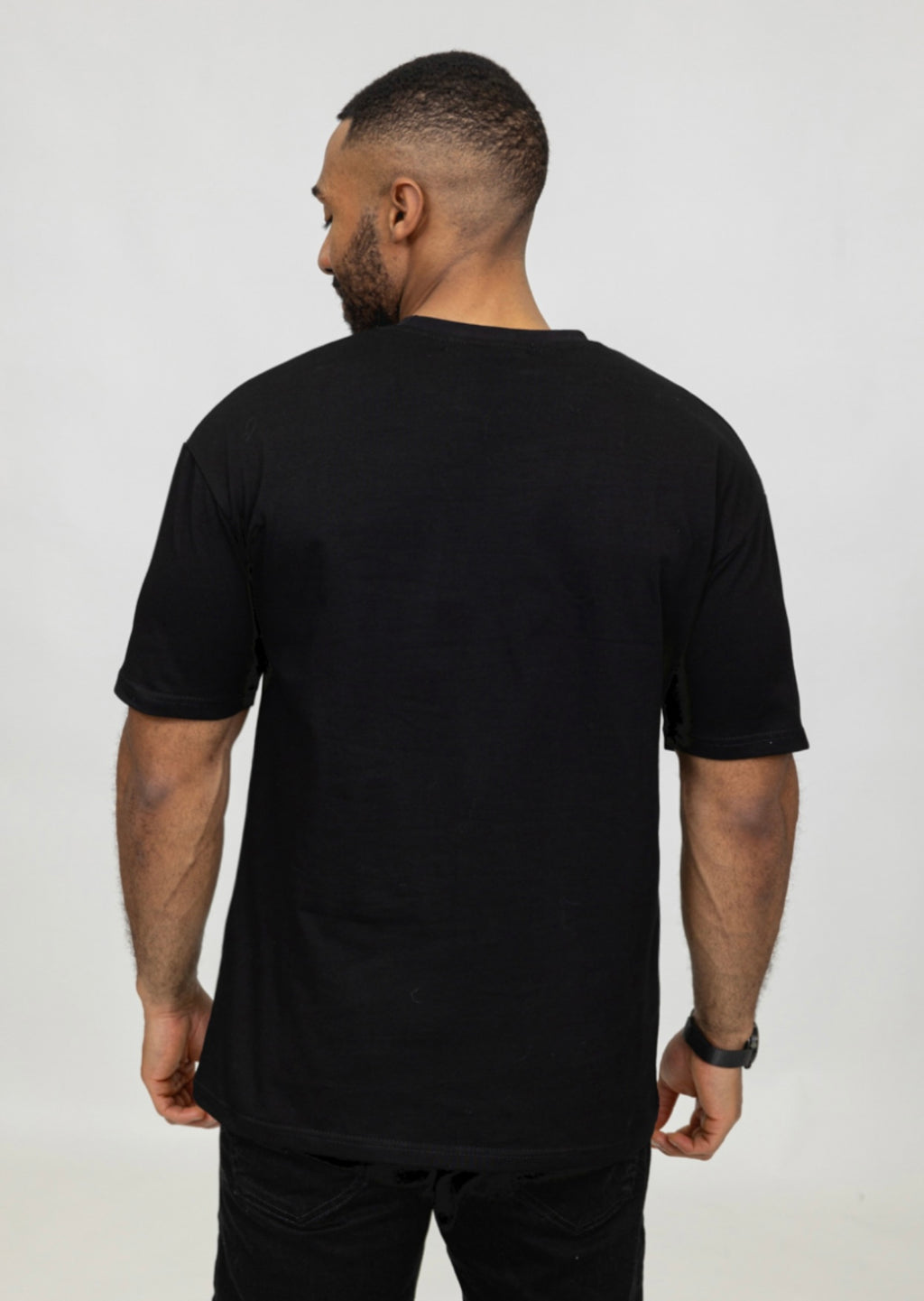 Zijaanzicht van model met zwart oversized T-shirt, achterkant en schoudernaden zichtbaar.