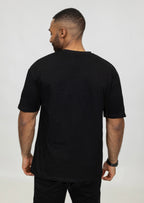 Zijaanzicht van model met zwart oversized T-shirt, achterkant en schoudernaden zichtbaar.