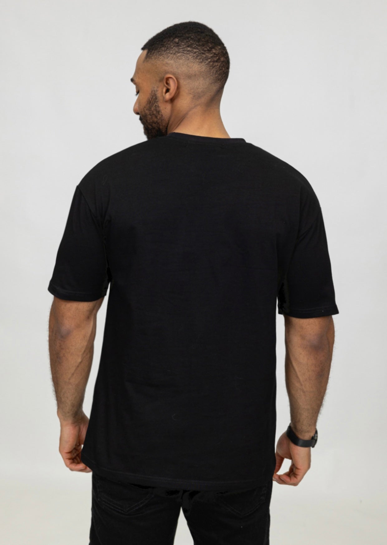 Zijaanzicht van model met zwart oversized T-shirt, achterkant en schoudernaden zichtbaar.