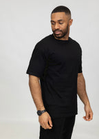 Model in zwart oversized T-shirt vanaf de zijkant, relaxte fit zichtbaar.