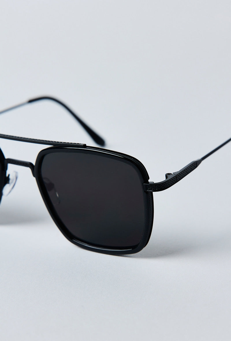 Close-up van de zwarte zonnebril met donkere UV400 glazen en metalen frame-detailshot voorkant.